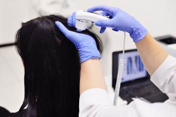doctor dermatologist diagnoses the structure of the hair of a young pretty girl with a special tool - a trichoscope. Trichology, trichogram