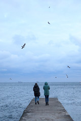 two young women walking on the pier in the sea in the winter day