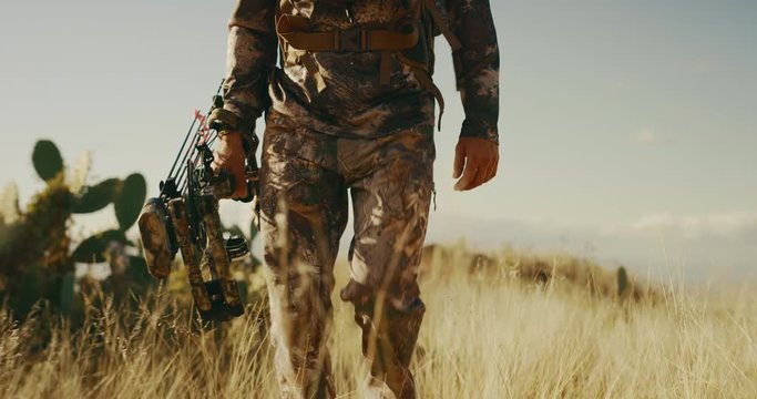 Chest down shot of bowhunter with compound bow in hand walking through golden prairie grass