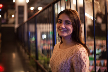 beautiful young woman with long hair in sweater sitting near railing in the mall