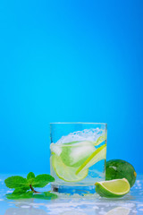 Splashing mojito cocktail with lime and fresh mint in glass on a blue background