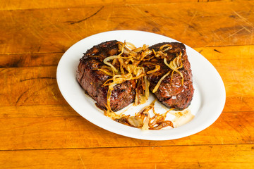 Prime Tenderloin Steaks Grilled and topped with sauteed onions resting on rustic cutting board