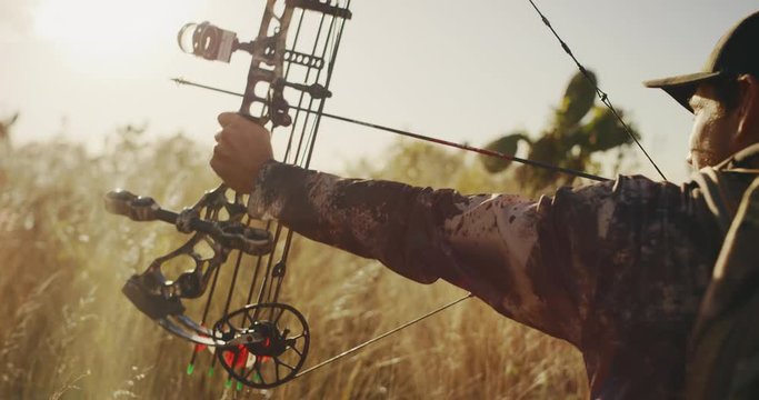 Medium close up of experienced bowhunter man drawing an arrow in the afternoon light