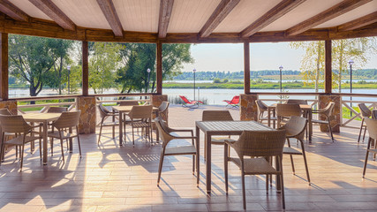 The restaurant with wicker, beautiful furniture is located on the bank of the river, lit by warm sunlight.