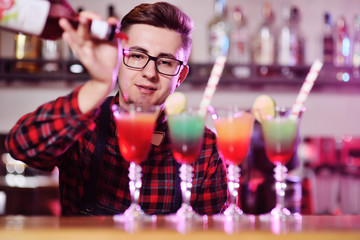 professional bartender prepares and mixes cocktails pouring red syrup from a bottle on the background of a bar in a nightclub