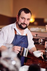 portrait of a handsome bearded barista preparing coffee on the background of a coffee shop and a coffee machine