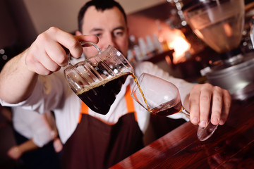 barista or coffee barman prepares coffee by an alternative method of brewing - pour over - by hot water spilling through a special filter with ground powder