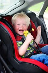 little baby boy with blond hair sitting in a red car seat and smiling