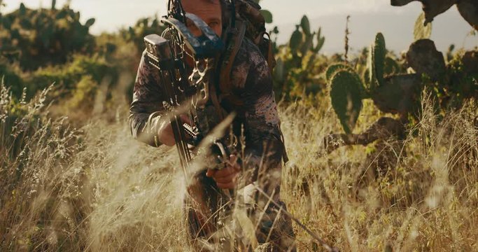 Experienced bowhunter crouches and creeps through tall grass with arrow knocked