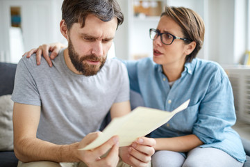 Confused man reading paper with answer to his application for job vacancy while his wife trying to reassure him