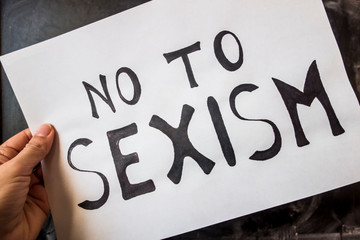 Female hand holding a white sheet of paper with the inscription - No To Sexism.