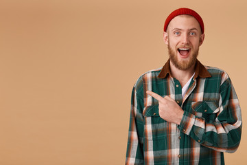 Indoor shot of amazed excited man feels successful, pointing at left corner on blank copy space, dropping jaw standing rightside isolated over beige background, says omg or wow.