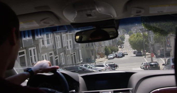 Man driving car down steep hill street during summer time - view from the back seat over the shoulder