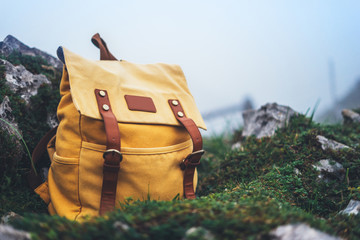 Hipster hiker tourist yellow backpack on background green grass nature in mountain, blurred...