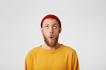 The bearded guy looks at the top with surprise, mouth rounded. Portrait of a man in a red cap...