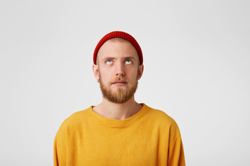 Close up of a guy with a slight smile, surprise, looks up at the empty space for copy. Bearded man with a fascinated look raised his head up saw something unusual isolated on white background
