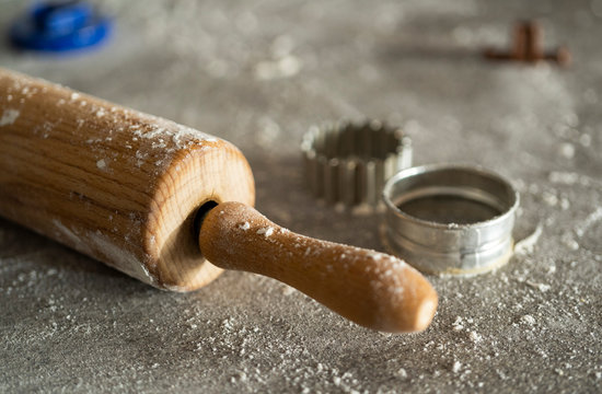 a rolling pin and cutting equitment for cutting out cookies of the biscuit dough on a kitchen table with a lot of flour