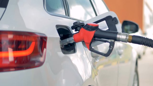 Fuel pistol with a red handle is refilling a white car