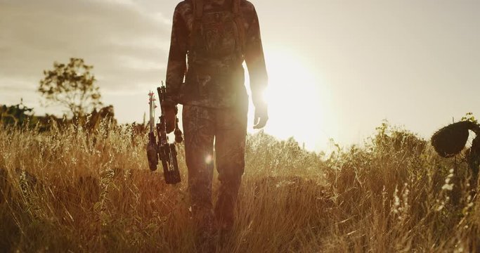 Bowhunter walking through golden grass at sunset