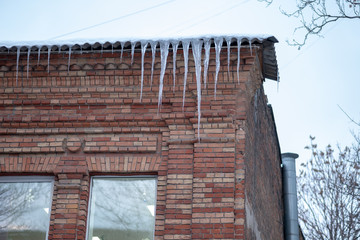 Large beautiful icicles melt on the roof of the house. Snow is melting. The ice is melting.