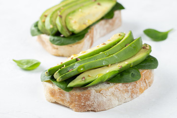 Two ciabatta toast with sliced avocado olive oil, spinach and flax and sesame seeds. Healthy vegetarian Breakfast on white background