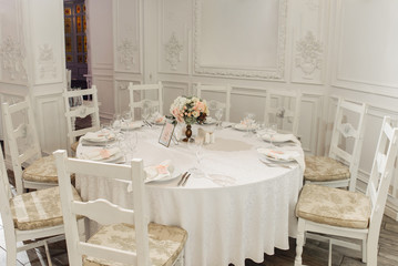 Festive round table which is beautifully decorated in pastel colors, with white plates, and a beautiful composition of roses in the center of table
