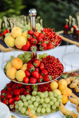 Hill of the fresh fruits on the holiday table. Strawberries, grapes, peaches, red currants outdoors