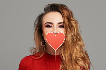 Beauty joyful Young fashion model Girl with Valentine Heart shaped  in her hands. Love Concept. Beautiful smiling young woman on grey background. Space for text