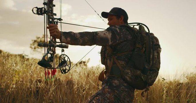 Orbit shot of experienced bowhunter backlit with golden light and arrow drawn