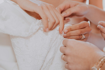 Bride's hands unbuttoning wedding dress with help