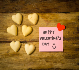 Happy Saint valentines day with post it note and heart shaped chocolate frame on wooden table