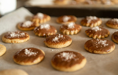 a lot of baked cookies and gingerbread on baking tray, decorated with chocolate and coconut flakes