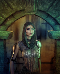 A beautiful warrior girl with a sword and in armor. A model in a chain skirt and a vest in a...