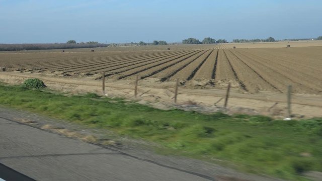 Slow motion passenger view. Passing ploughed fields ready for planting. Fresno County, California, USA.