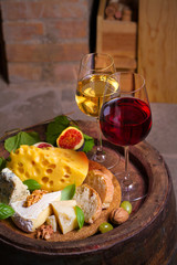 Glasses of red and white wine with cheese, bread and nuts on old cask in wine cellar. vertical