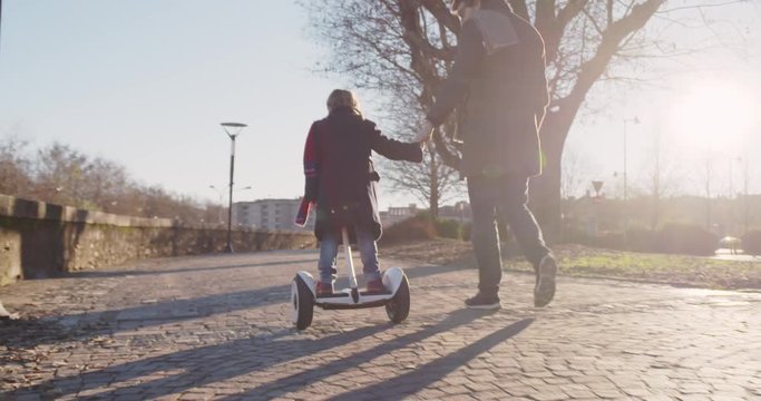Daughter child girl learning segway riding with dad teaching in city.Modern future transport technology.Active safety family.Sidewalk urban outdoor.Warm sunset cold backlight.4k slow motion 60p video
