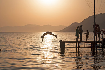Man jumping over a pier into the sea on sunset in marmaris, Turkey. Vintage effect. No fear, courage, brave, dare concept.