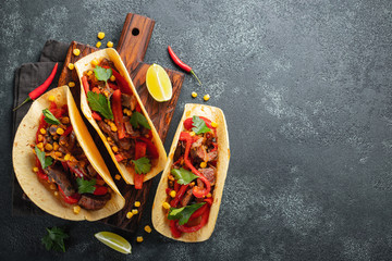 Mexican tacos with beef, vegetables and salsa. Tacos al pastor on wooden board on black background....