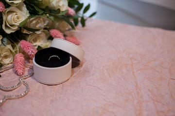 engagement ring in a round white box on a pink paper background and with a bouquet of white roses and a lagurus