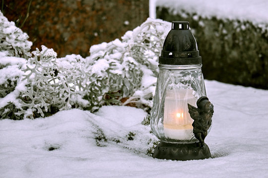 Lantern with candle at the grave covered with snow in winter