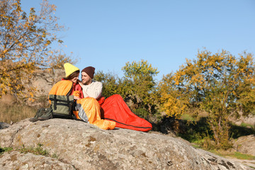 Fototapeta premium Couple of campers in sleeping bags sitting on rock. Space for text
