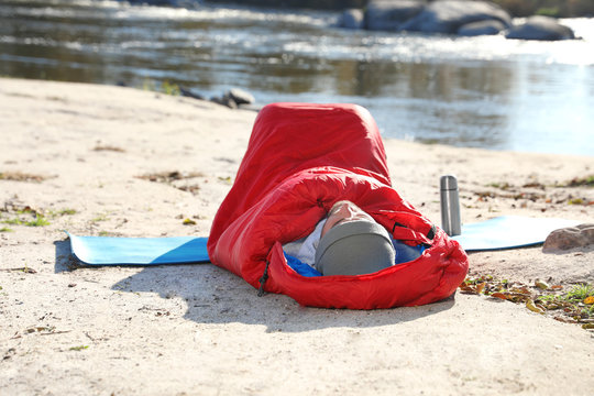 Male camper lying in sleeping bag on wild beach