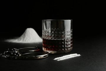 Glass of alcohol, cocaine and handcuffs on dark table