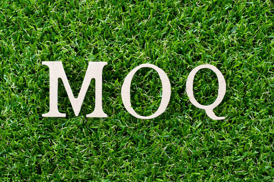 Wood letter in word MOQ (Abbreviation of Minimum Order Quantity) on artificial green grass background