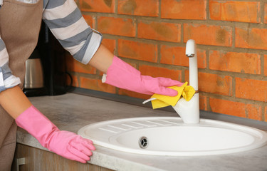 Woman cleaning tap with rag in kitchen, closeup