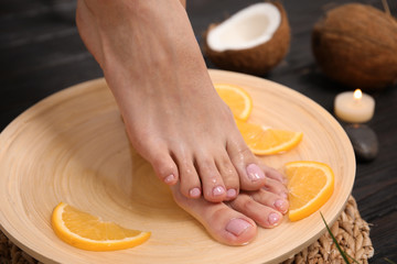 Obraz na płótnie Canvas Woman soaking her feet in plate with water and orange slices on wooden floor, closeup. Spa treatment