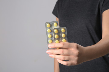 Woman holding pills in blister packs on gray background, closeup. Space for text