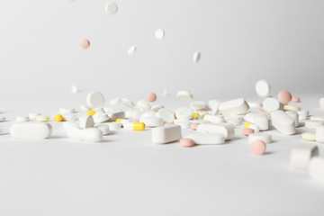 Different pills falling on table against white background