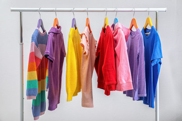 Colorful clothes hanging on wardrobe rack against light background
