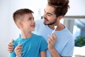 Young man and his son with toothbrushes in bathroom. Personal hygiene
